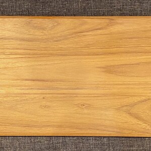 May include: A rectangular wooden cutting board with a light brown finish. The wood grain is visible, and the board has a slightly raised edge. The cutting board is approximately 18 inches long and 8 inches wide.