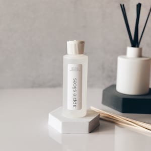 May include: A clear glass bottle with a white cap and label. The label reads "en mer" and "apple slices". The bottle is sitting on a white hexagonal stand.