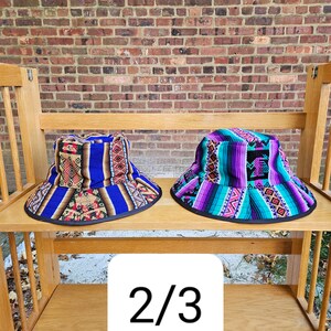 K&ouml;nnte beinhalten: Zwei bunte Bucket-Hats mit geometrischen Mustern. Der Hut links ist blau, lila und rot. Der Hut rechts ist lila, t&uuml;rkis und wei&szlig;. Die H&uuml;te befinden sich auf einem Holzregal mit der Nummer 2/3 auf einem wei&szlig;en Quadrat.