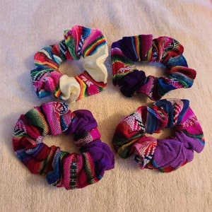May include: Four colorful fabric scrunchies with a woven pattern in shades of pink, purple, blue, and green. The scrunchies are made of a soft, stretchy fabric and are perfect for holding hair in place.