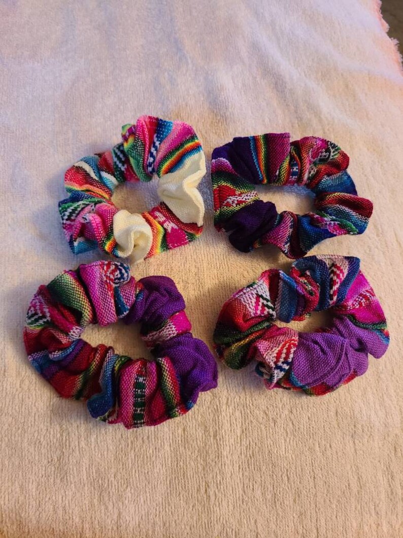May include: Four colorful fabric scrunchies with a woven pattern in shades of pink, purple, blue, and green. The scrunchies are made of a soft, stretchy fabric and are perfect for holding hair in place.