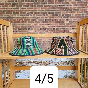 K&ouml;nnte beinhalten: Zwei bunte gewebte Bucket-Hats mit schwarzem Besatz, auf einem Holzregal ausgestellt mit dem Text "4/5" auf einem wei&szlig;en Quadrat.
