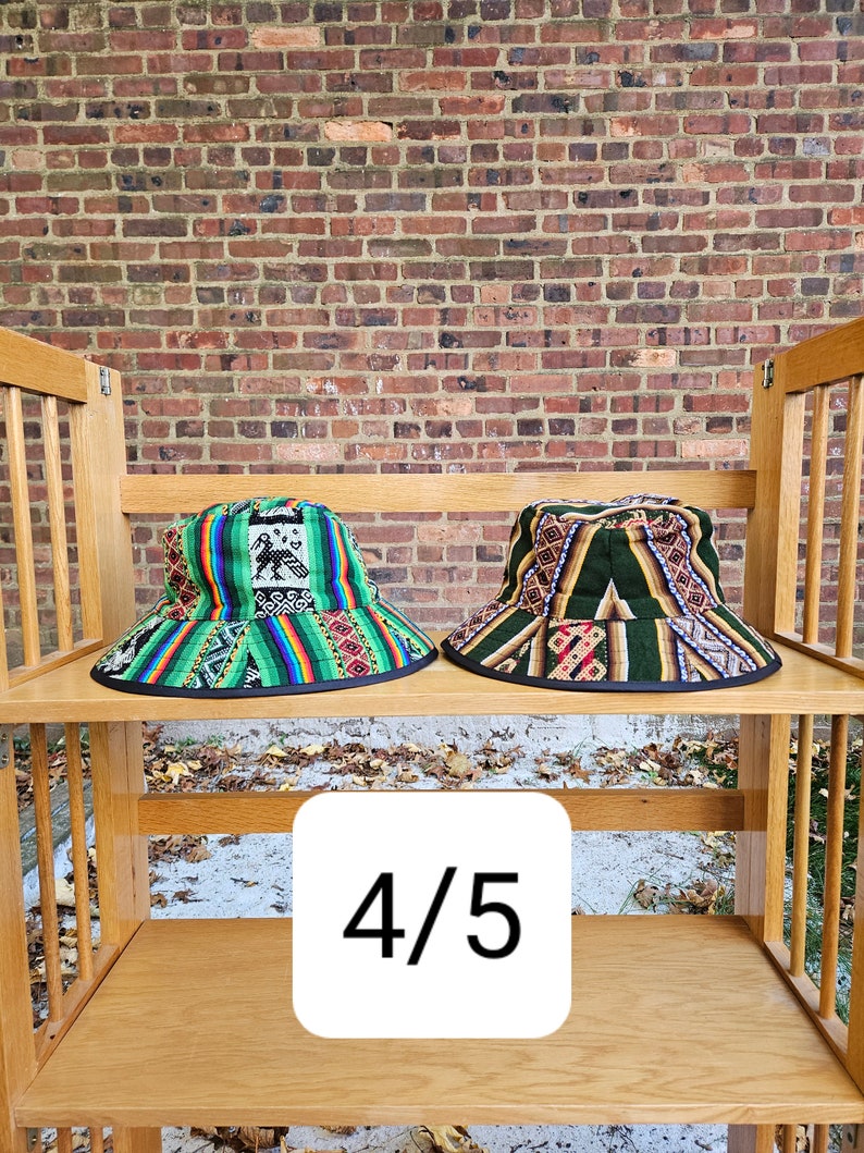 K&ouml;nnte beinhalten: Zwei bunte gewebte Bucket-Hats mit schwarzem Besatz, auf einem Holzregal ausgestellt mit dem Text "4/5" auf einem wei&szlig;en Quadrat.