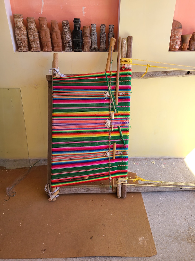May include: A wooden loom with colorful yarn woven into a striped pattern. The loom is made of wood and has a simple design. The yarn is a variety of colors, including red, green, yellow, and blue.