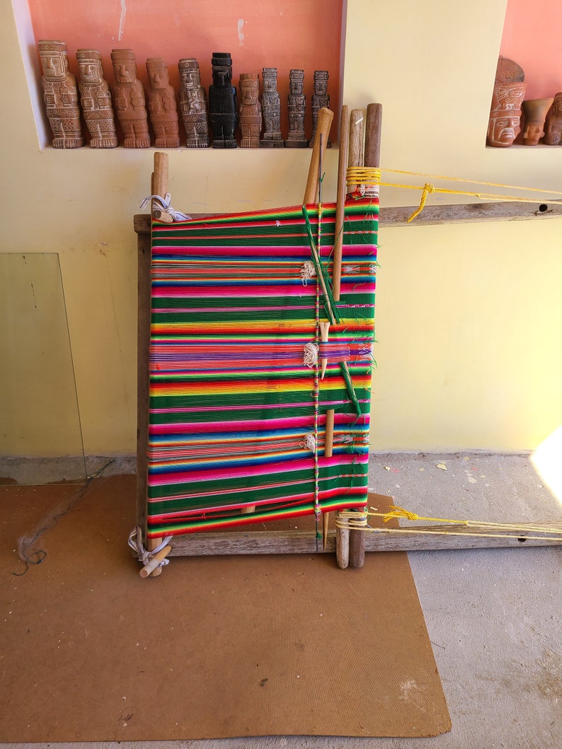 Puede incluir: Un telar de madera con hilo de colores tejido en un patr&oacute;n de rayas. El telar est&aacute; hecho de madera y tiene un dise&ntilde;o simple. El hilo es de varios colores, incluyendo rojo, verde, amarillo y azul.