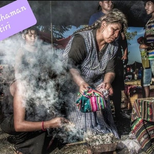 May include: A woman in a plaid shirt and a colorful woven shawl performs a traditional Bolivian Shaman Yatiri ceremony. Smoke rises from a burning offering in a metal bowl. The woman is surrounded by people and a table covered in a patterned cloth.