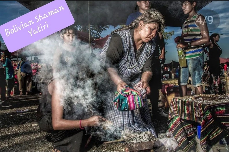 May include: A woman in a plaid shirt and a colorful woven shawl performs a traditional Bolivian Shaman Yatiri ceremony. Smoke rises from a burning offering in a metal bowl. The woman is surrounded by people and a table covered in a patterned cloth.