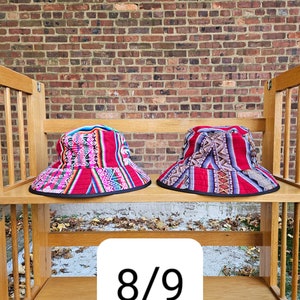 K&ouml;nnte beinhalten: Zwei bunte Bucket-Hats mit geometrischen Mustern in Rot, Pink, Blau und Schwarz auf einem Holzregal. Der Text "8/9" ist auf dem Regal sichtbar.