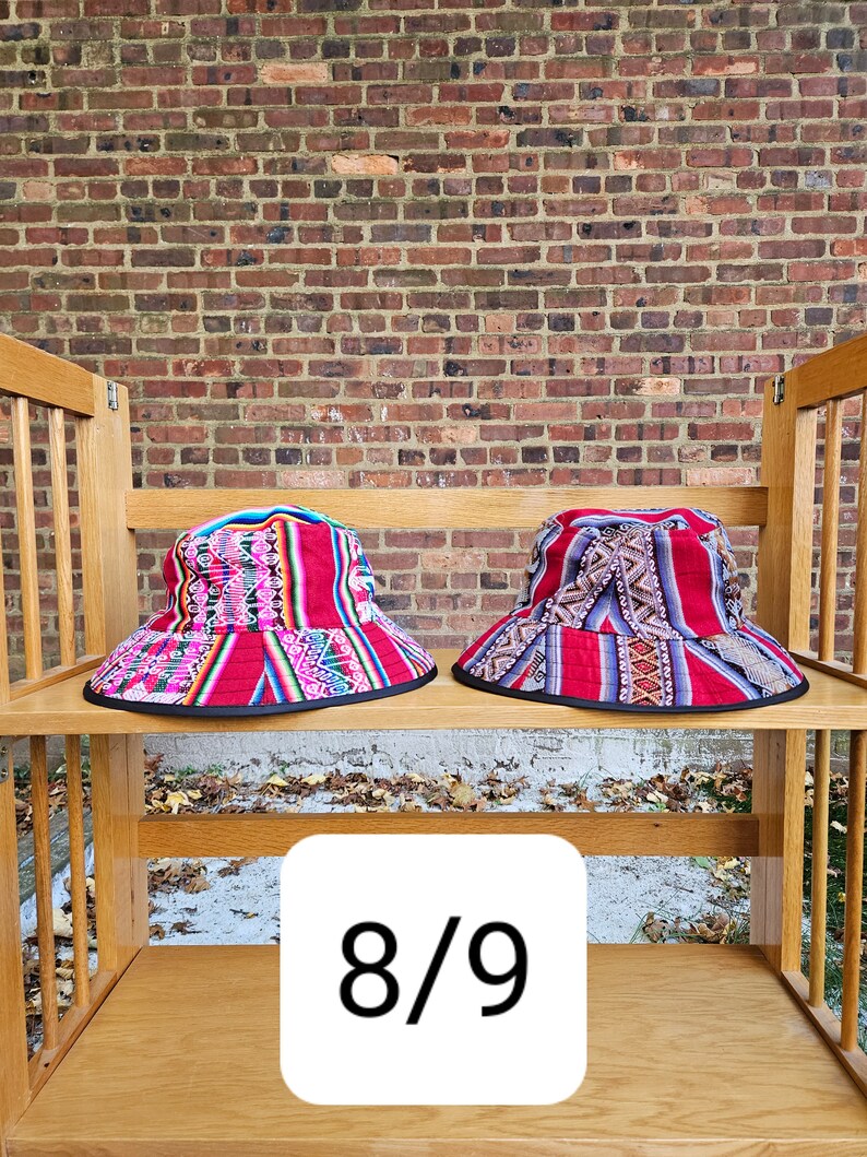 K&ouml;nnte beinhalten: Zwei bunte Bucket-Hats mit geometrischen Mustern in Rot, Pink, Blau und Schwarz auf einem Holzregal. Der Text "8/9" ist auf dem Regal sichtbar.
