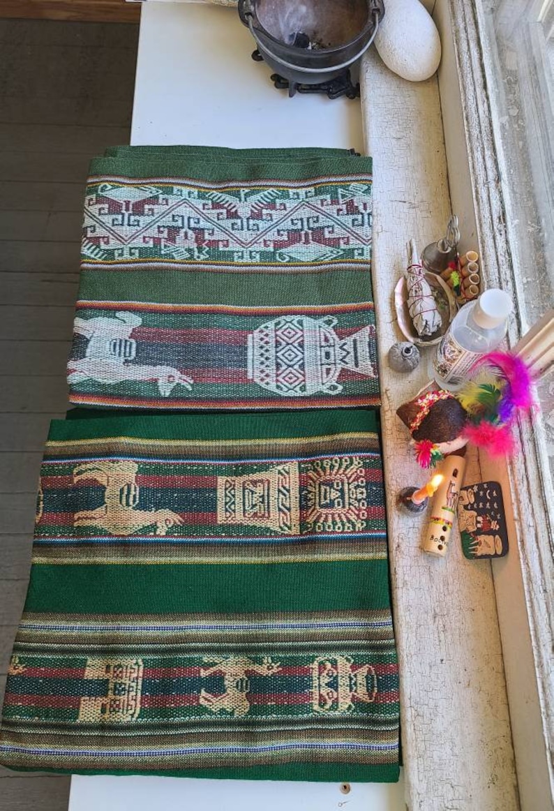 Puede incluir: Tres textiles tejidos en verde y marr&oacute;n con intrincados patrones, incluyendo llamas, dise&ntilde;os geom&eacute;tricos y un jarr&oacute;n estilizado. Los textiles est&aacute;n dispuestos sobre una superficie blanca con otros objetos, incluyendo una flauta de madera, una vela y una pluma.
