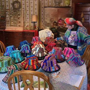 K&ouml;nnte beinhalten: Eine Sammlung bunter, gemusterter Bucket-Hats mit verschiedenen Designs. Die H&uuml;te sind auf einem Tisch mit einer wei&szlig;en Tischdecke angeordnet.