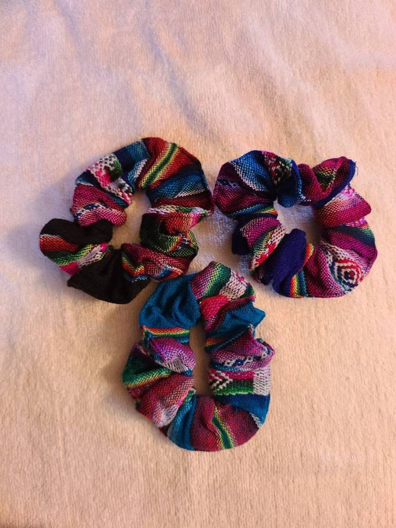 May include: Three colorful hair scrunchies with a woven pattern. The scrunchies are made of fabric and have a variety of colors, including pink, blue, green, and black.
