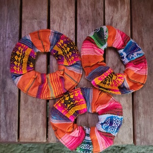 May include: Three colorful fabric hair scrunchies with a woven pattern in shades of orange, pink, blue, green, and yellow.