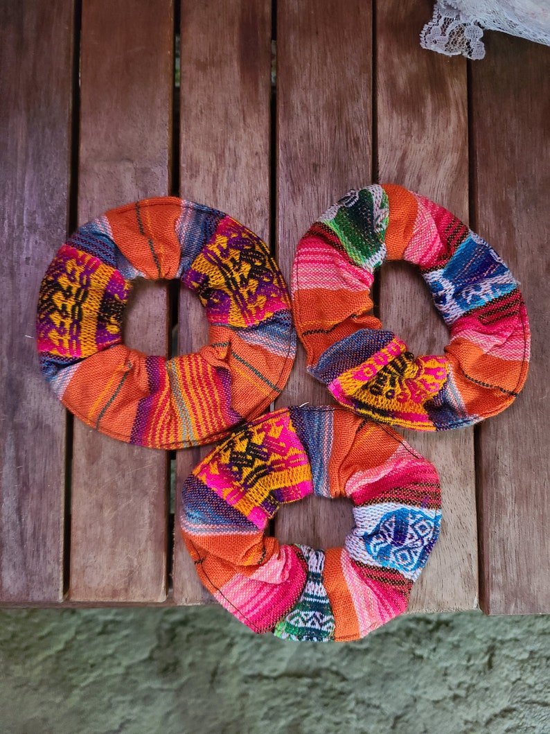 May include: Three colorful fabric hair scrunchies with a woven pattern in shades of orange, pink, blue, green, and yellow.