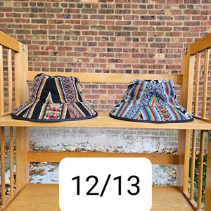 K&ouml;nnte beinhalten: Zwei bunte gewebte Bucket-Hats auf einem Holzregal mit der Nummer 12/13 auf einem wei&szlig;en Etikett.