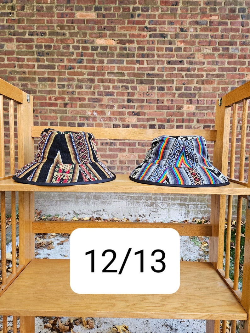K&ouml;nnte beinhalten: Zwei bunte gewebte Bucket-Hats auf einem Holzregal mit der Nummer 12/13 auf einem wei&szlig;en Etikett.