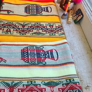 Puede incluir: Un conjunto de cuatro textiles tejidos coloridos con patrones geom&eacute;tricos e im&aacute;genes de vasijas estilizadas. Los textiles est&aacute;n dispuestos en una pila, con el textil superior de color amarillo brillante.