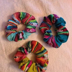 May include: Three colorful scrunchies with a woven pattern. The scrunchies are made of fabric and have a variety of colors, including pink, green, blue, yellow, and red.