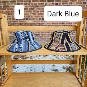 K&ouml;nnte beinhalten: Zwei Bucket-Hats auf einem Holzregal. Der Hut links ist dunkelblau mit einem bunten geometrischen Muster. Der Hut rechts ist schwarz mit einem bunten geometrischen Muster. Der Text "1" und "Dark Blue" ist &uuml;ber den H&uuml;ten sichtbar.