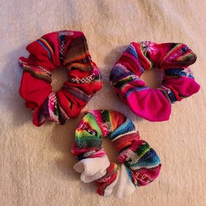 May include: Three colorful scrunchies with a variety of patterns. The scrunchies are made of fabric and have a gathered look.