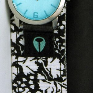 May include: A black and white patterned watch band with a silver watch face and blue hands. The watch face has the word "FOSSIL" printed on it.