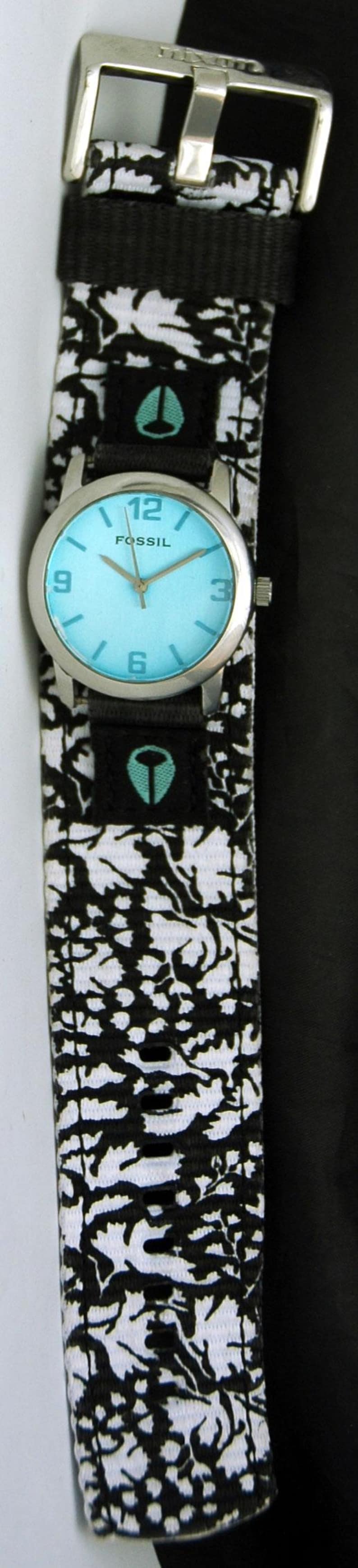 May include: A black and white patterned watch band with a silver watch face and blue hands. The watch face has the word "FOSSIL" printed on it.