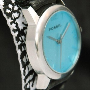 May include: A silver Fossil wristwatch with a blue face and black and white patterned band. The watch face has silver hands and the word "FOSSIL" printed in black.