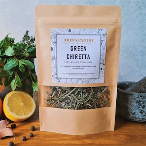 May include: A brown paper bag of Green Chiretta herbs with a clear window, labelled "John's Pantry." The label includes the text "Green Chiretta Andrographis Paniculata." The image also shows lemons, garlic, peppercorns, and a mortar and pestle.