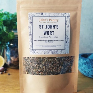 May include: A brown paper bag of St John's Wort herbs with a clear window. The label reads "John's Pantry Herbs and Spices" and "ST JOHN'S WORT". The bag is filled with dried herbs. Other ingredients are visible in the background.