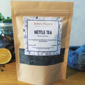 May include: A brown paper bag with a white label that says "John's Pantry Herbs and Spices" and "Nettle Tea Urtica Dioica". The label also includes instructions for brewing the tea: "Use 1-2 teaspoons per 1 cup of boiling water and steep for 10-20 min. Strain off and enjoy."