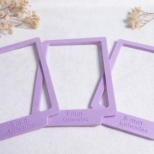 Puede incluir: Tres marcos rectangulares de color lavanda con esquinas redondeadas están dispuestos sobre una superficie blanca. Cada marco tiene una pestaña con la medida y la palabra "Ambrodec" impresa. Las medidas son 3 mm, 4 mm y 5 mm.