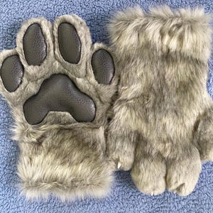 May include: A pair of gray furry paw-shaped hand warmers. The hand warmers have a textured, black paw print design.
