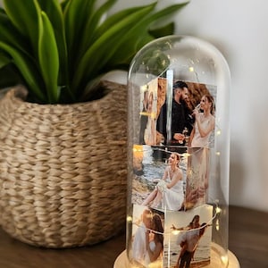 May include: A glass dome with a wooden base houses several photos illuminated by fairy lights. The photos depict couples in various settings. A potted plant in a woven basket sits to the left of the dome.