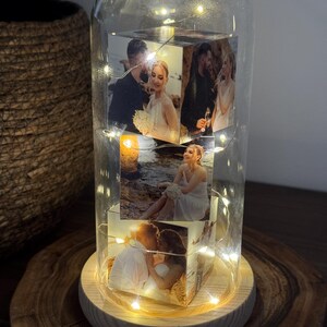 May include: A decorative glass dome with a wooden base, housing a rotating cube displaying four photographs. The cube is illuminated by string lights. The photos appear to be of a couple, possibly a wedding or engagement theme.