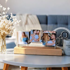 May include: A wooden photo display with three rotating photo cubes. Each cube displays a different photo. The display sits on a light-colored wooden base with silver metal supports. The photos appear to be of a couple.
