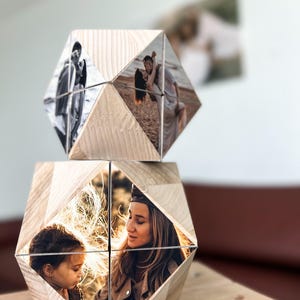 May include: Two wooden photo cubes with geometric shapes. The top cube has photos of a couple on a beach. The bottom cube has photos of a woman and a child.