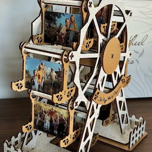 Könnte beinhalten: Ein hölzernes Riesenrad-Foto-Display mit Familienfotos. Das Rad besteht aus hellbraunem Holz mit weißen Akzenten und einem dekorativen Sockel. Der Text "The Magic Wheel of Memories" ist sichtbar.