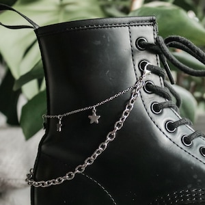 May include: Black leather ankle boots with a silver chain and star charms attached to the laces.