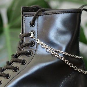 May include: Black leather boot with a silver chain accessory. The chain is attached to the top of the boot and hangs down the side.