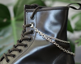 May include: Black leather boot with a silver chain accessory. The chain is attached to the top of the boot and hangs down the side.