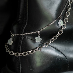 May include: A pair of silver chains with star-shaped charms hanging from them. The chains are draped over a black leather boot.