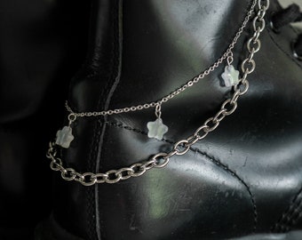May include: A pair of silver chains with star-shaped charms hanging from them. The chains are draped over a black leather boot.