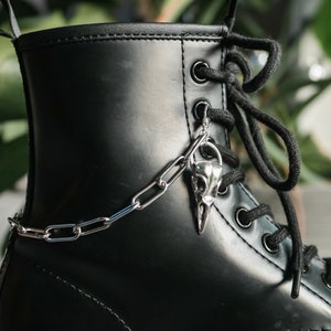 May include: Black leather boot with a silver chain and a bird skull charm attached to the laces.