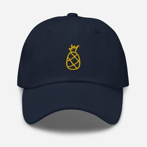 Könnte beinhalten: Eine marineblaue Baseballkappe mit einem gestickten Ananas-Motiv in Gelb.