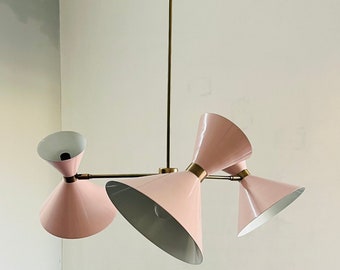 May include: A pink and brass chandelier with four light fixtures. The light fixtures are shaped like cones and have a white interior.