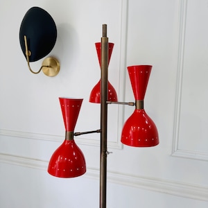 May include: A brass floor lamp with three red, cone-shaped lampshades. The lamp has a long, slender stem and a round base.