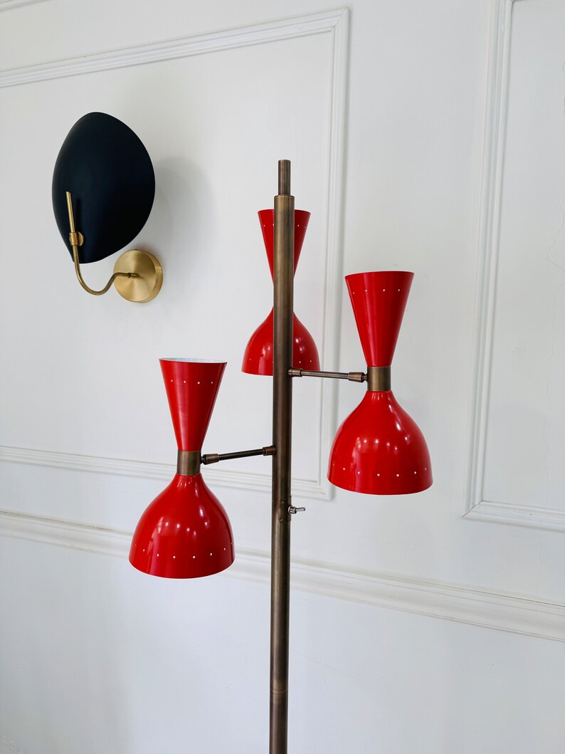 May include: A brass floor lamp with three red, cone-shaped lampshades. The lamp has a long, slender stem and a round base.