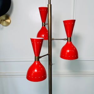 May include: A brass floor lamp with three red and white shades. The lamp has a long, slender stem and a round base.