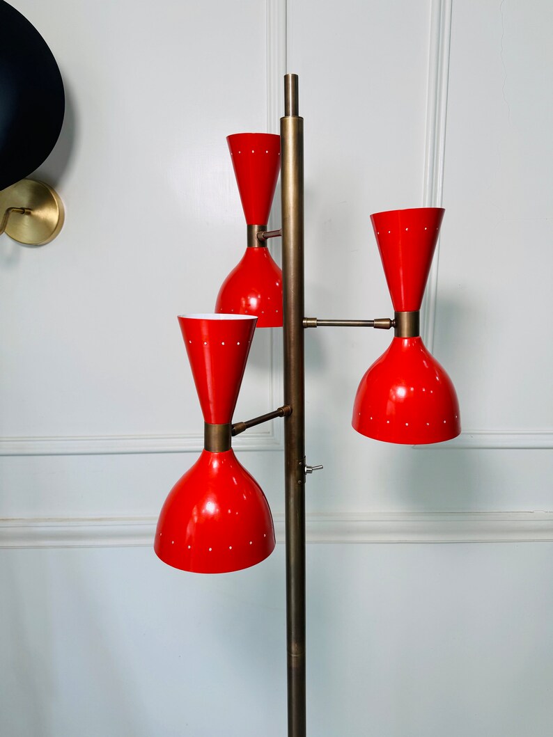May include: A brass floor lamp with three red and white shades. The lamp has a long, slender stem and a round base.