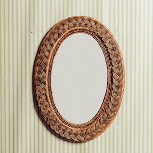 May include: A woven wicker oval mirror with a natural brown finish. The mirror has a simple, elegant design and would look great in a variety of settings.